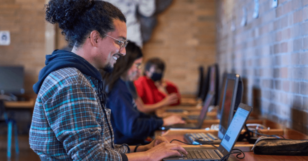 Imagen de un hombre sonriendo al frente de un computador portátil 