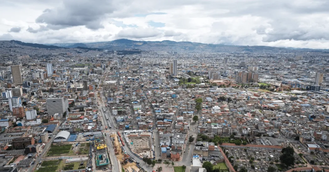 Vista panorámica de Bogotá con edificaciones, vías principales y los cerros orientales al fondo bajo un cielo nublado.