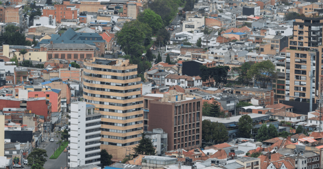Vista panorámica de Bogotá con edificios residenciales y comerciales de diferentes alturas en primer plano, y los Cerros Orientales en un día nublado.