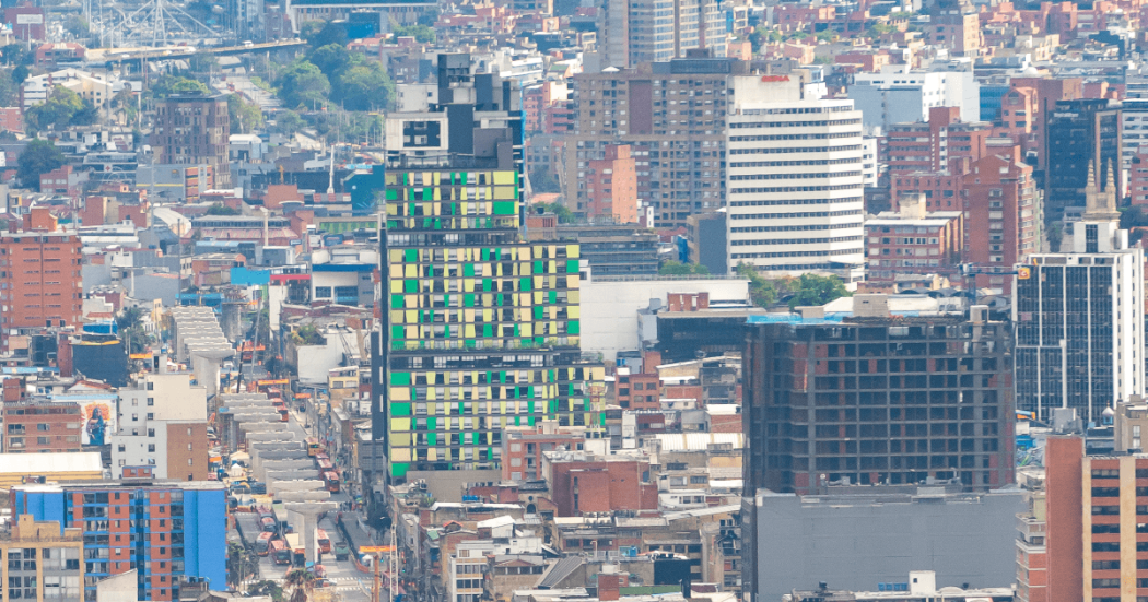 Vista panorámica del centro de Bogotá con edificios de diferentes alturas, una torre de fachada verde y amarilla en primer plano, vías urbanas y construcciones residenciales y comerciales densamente agrupadas.