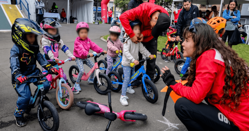 Niños y niñas de primera infancia participan en una actividad de push bike con bicicletas de equilibrio y cascos de protección en un espacio al aire libre en Bogotá.