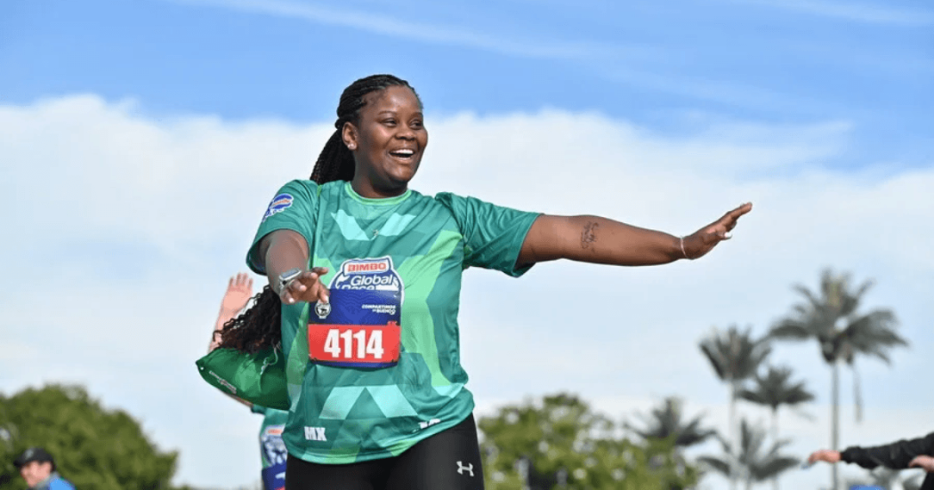 Persona participante de la Bimbo Global Race corre al aire libre con camiseta verde y dorsal 4114, con un brazo extendido durante la competencia.
