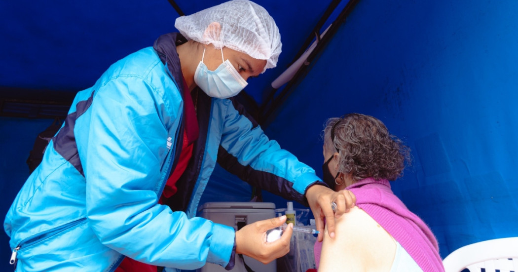 Foto que muestra un enfermero colocando una vacuna en un brazo a una mujer mayor.