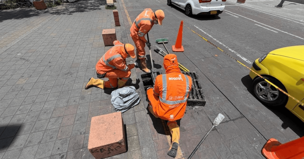 Foto que muestra tres personas con el uniforme de Aguas Bogotá limpiando un sumidero 