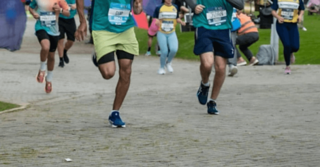 Primer plano de las piernas de varios corredores mientras participan en una carrera atlética sobre una vía pavimentada.