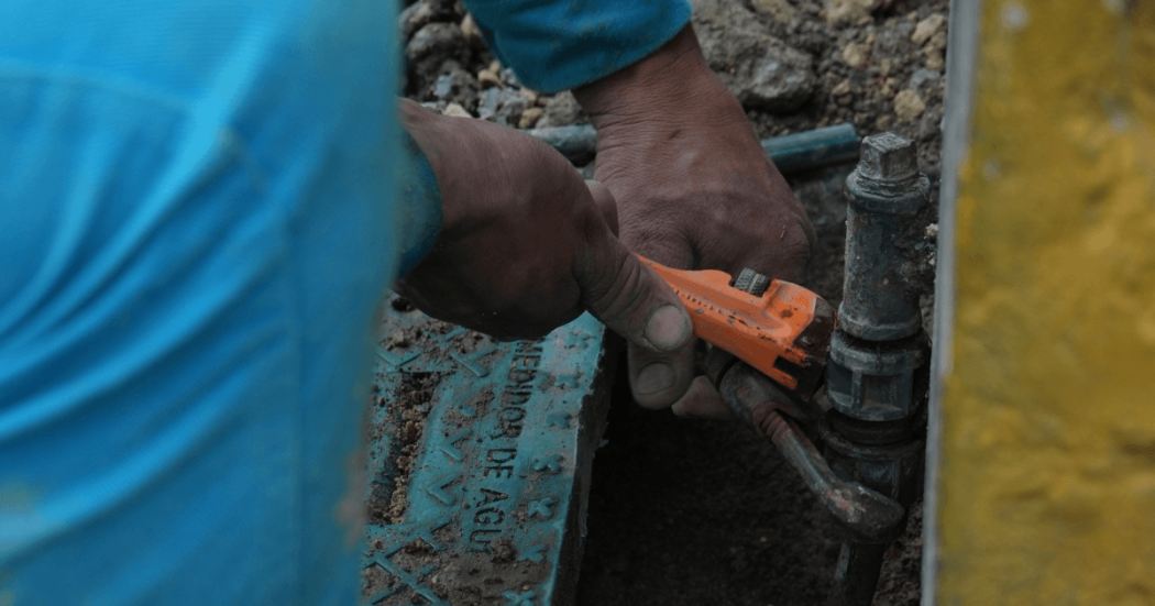 Foto que muestra unas manos con una llave arreglando un tubo de agua