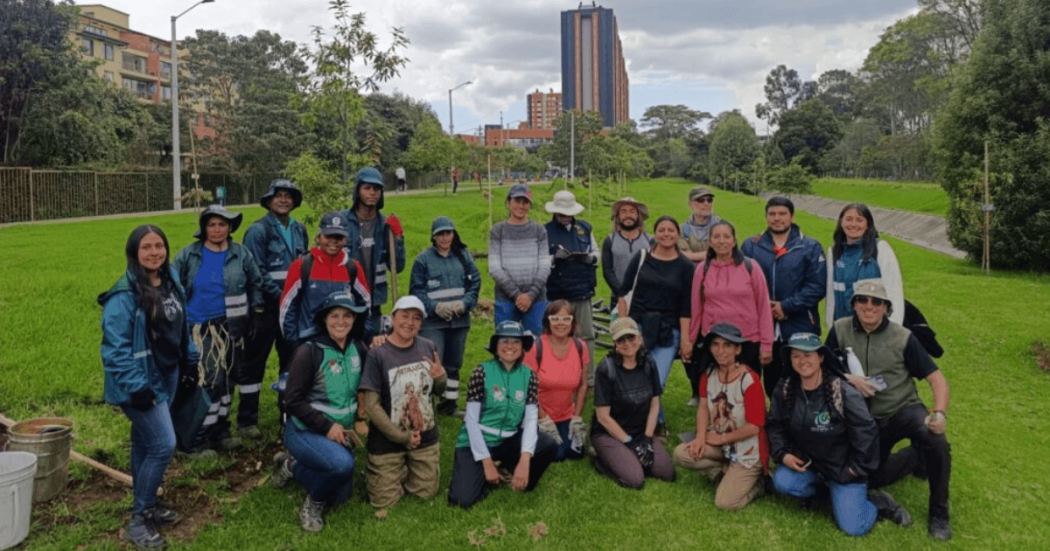 Grupo de personas posa para una fotografía al aire libre sobre una zona con césped. Varias personas llevan chalecos, gorras y prendas de colores llamativos, mientras algunas sostienen herramientas utilizadas en actividades de jardinería o mantenimiento vegetal.