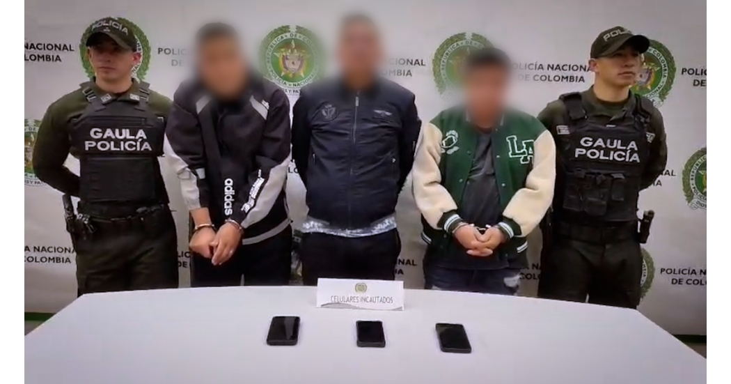 Foto de tres hombres capturados por la policía, escoltados por dos oficiales, uno en cada costado. 