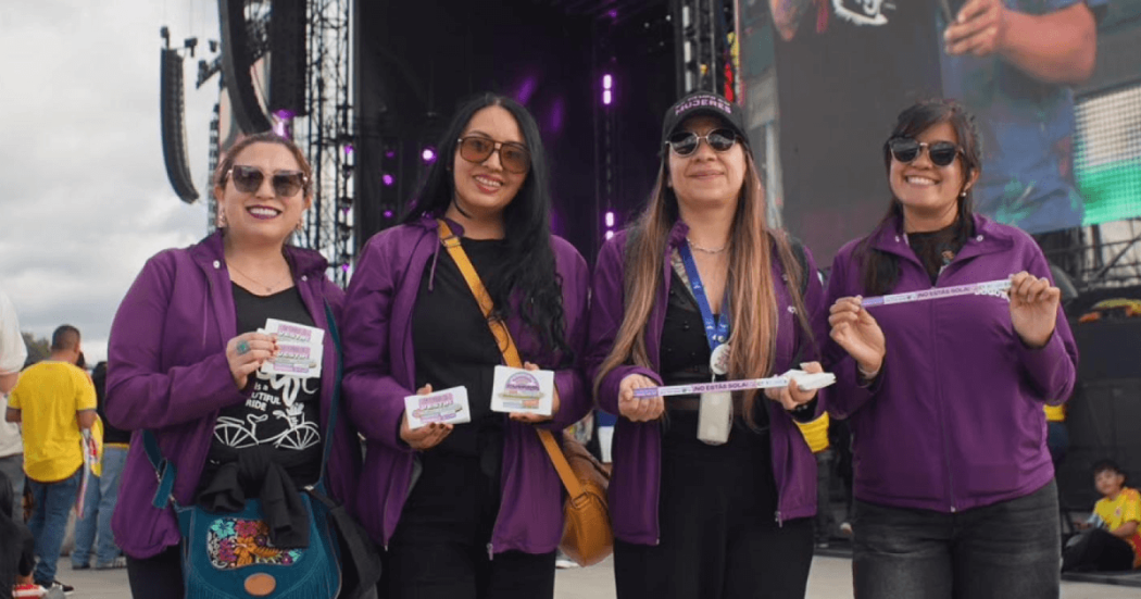Cuatro mujeres con chaqueta morada de la Secretaría de la Mujer en un concierto.