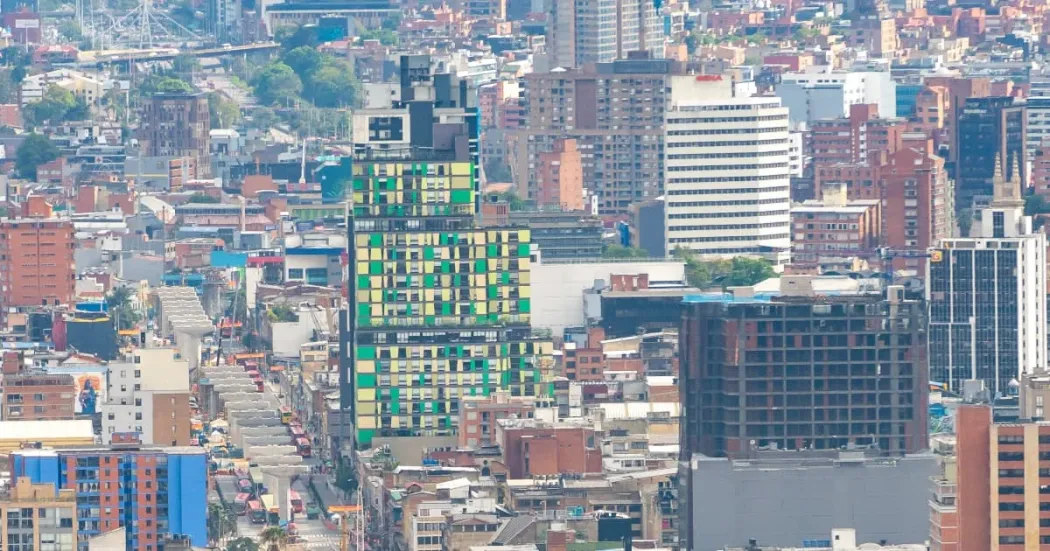 Vista panorámica del centro de Bogotá con edificios de diferentes alturas; en primer plano, una fachada intervenida con paneles verdes y amarillos entre construcciones urbanas.