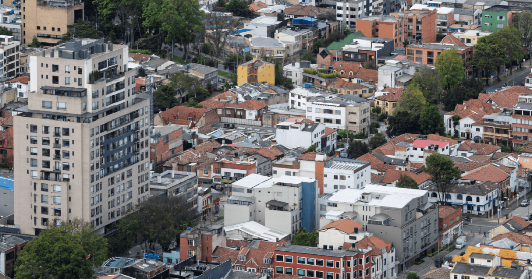 Vista aérea de un sector residencial y comercial de Bogotá, con edificios de mediana y gran altura, viviendas de teja roja y áreas arborizadas.