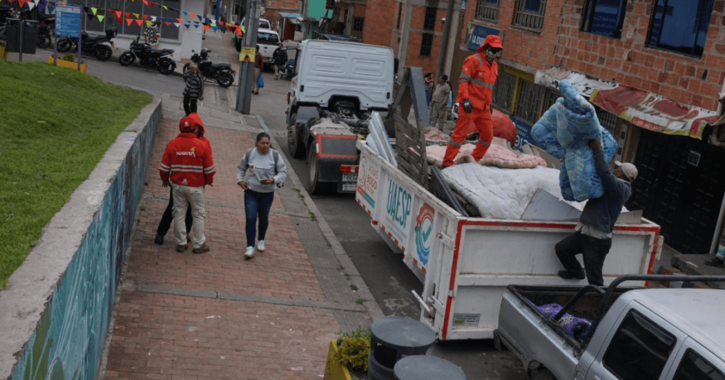 Foto que muestra un carro recolector de basura y personas caminando en la calle 