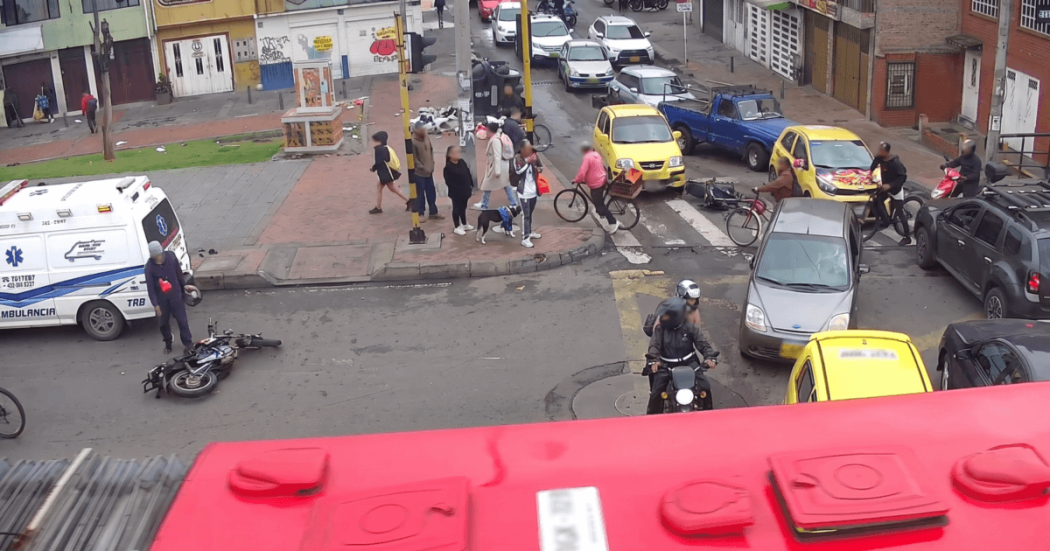 Ambulancia junto a una motocicleta caída en una intersección de la avenida Caracas con calle 33 Sur, mientras ciudadanos, ciclistas, motociclistas y vehículos permanecen en el lugar.