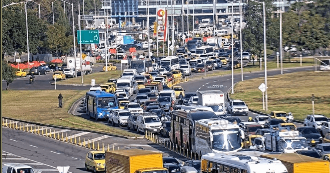 Alta congestión vehicular en avenida El Dorado de Bogotá con filas de carros, buses, camiones y motocicletas avanzando lentamente entre varios carriles. Se observan separadores viales, señalización y tránsito denso en ambos sentidos.