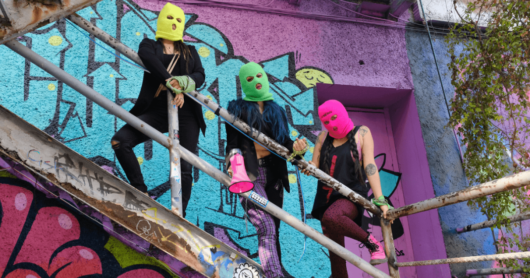 Imagen de tres mujeres con capcuhas de colores y un megáfono 