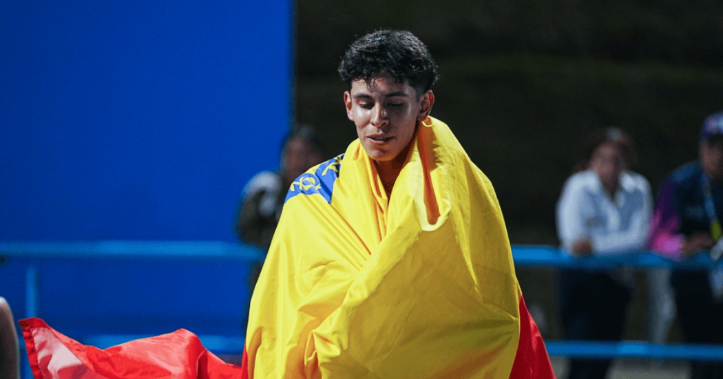Deportista envuelto en bandera de Bogotá durante una competencia deportiva, con parte de una pista azul visible al fondo.