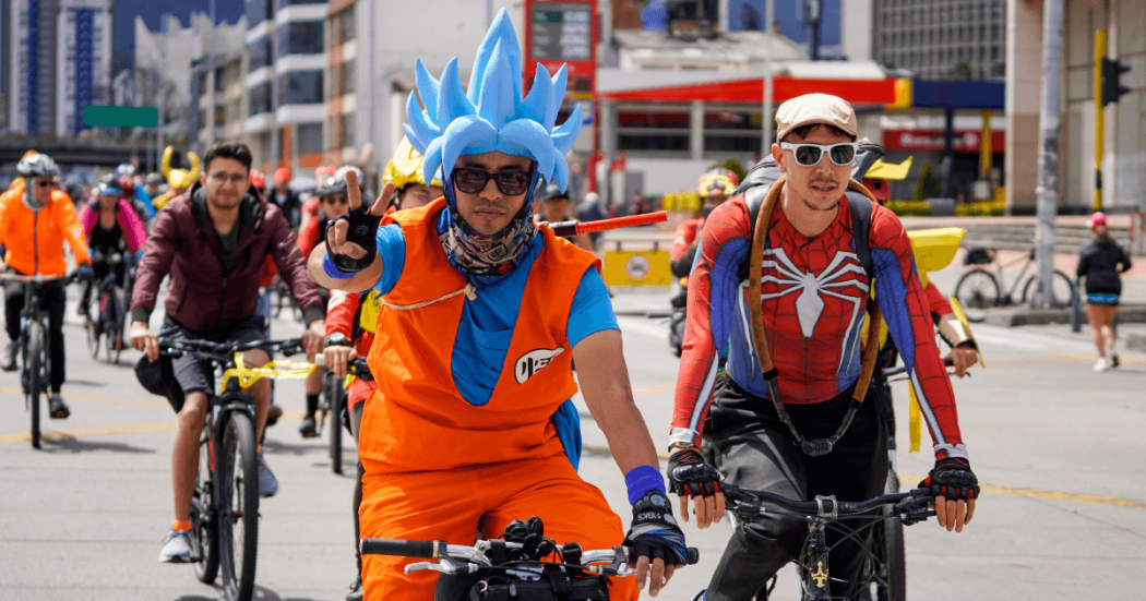 Personas disfrazadas de personajes de anime y superhéroes participan en una jornada de Recreovía en Bogotá, mientras recorren una avenida en bicicleta junto a decenas de ciclistas.