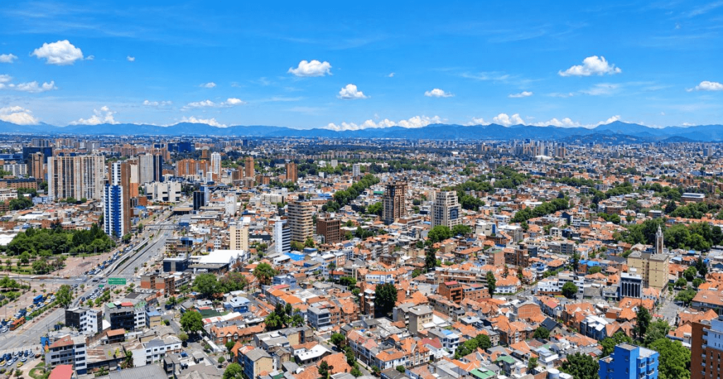 Vista panorámica de Bogotá desde gran altura, con una amplia zona urbana compuesta por viviendas de teja roja, edificios residenciales y vías vehiculares.