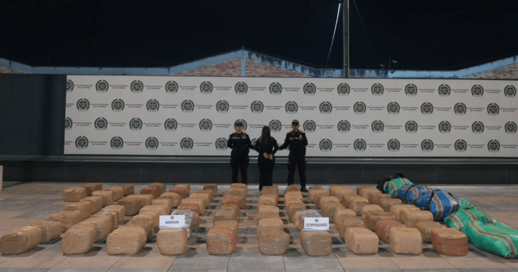 Foto de una persona capturada en medio de dos policías, con e cargamento de 700 kg de marihuana expuestos en el piso. 