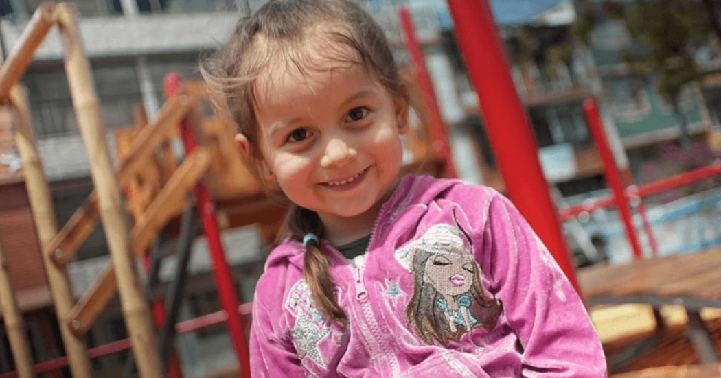 Foto de una niña sonriente con un saco rosado.