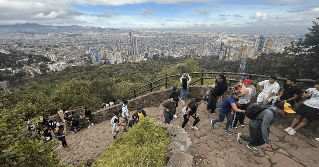 Vista panorámica de Bogotá desde un mirador en la montaña. Varias personas recorren y descansan en el sendero de Monserrate rodeado de vegetación