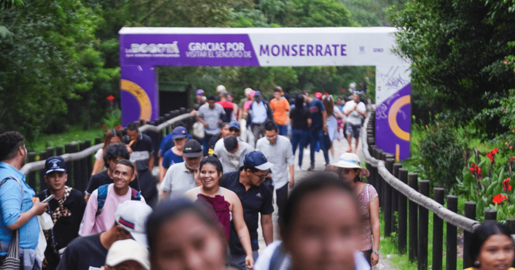 Decenas de personas recorren el sendero de Monserrate en Bogotá, pasando por un pórtico de ingreso ubicado en medio de vegetación y jardines a los costados del camino.