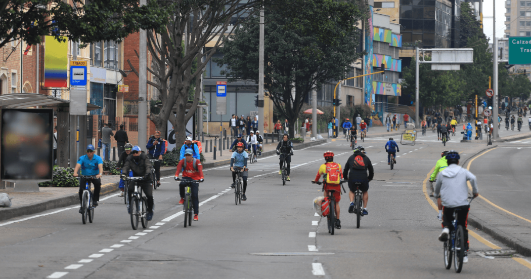 Ciclistas y peatones transitan por una vía de la Ciclovía de Bogotá, rodeados de árboles y edificaciones urbanas durante una jornada recreativa al aire libre
