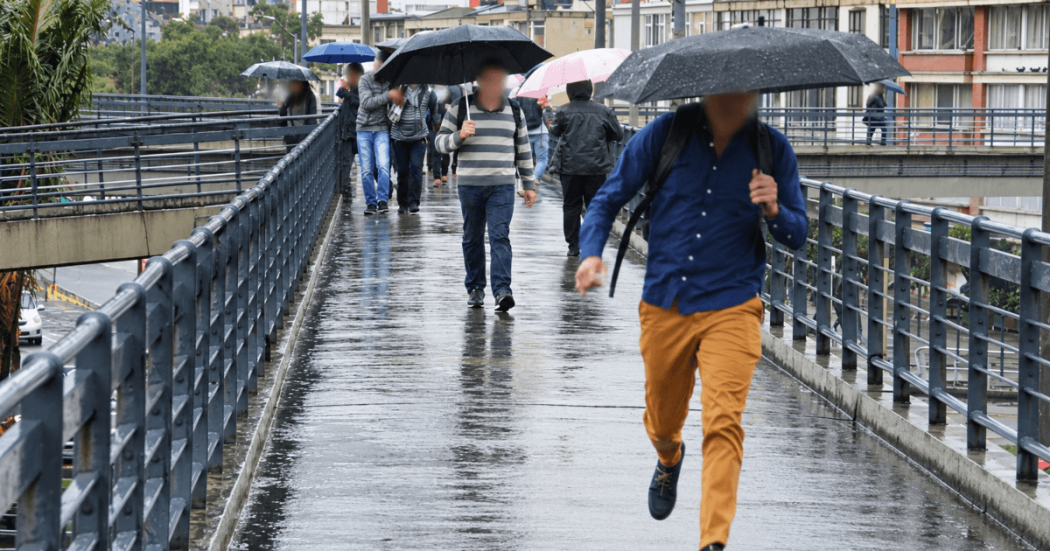 Personas caminan bajo la lluvia por una vía de Bogotá mientras una de ellas sostiene una sombrilla negra y otras transitan por un andén mojado durante fenómeno de El Niño 2026.