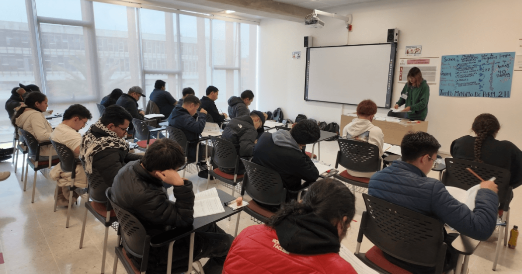 Foto que muestra personas sentadas en escritorios en un salón de clases