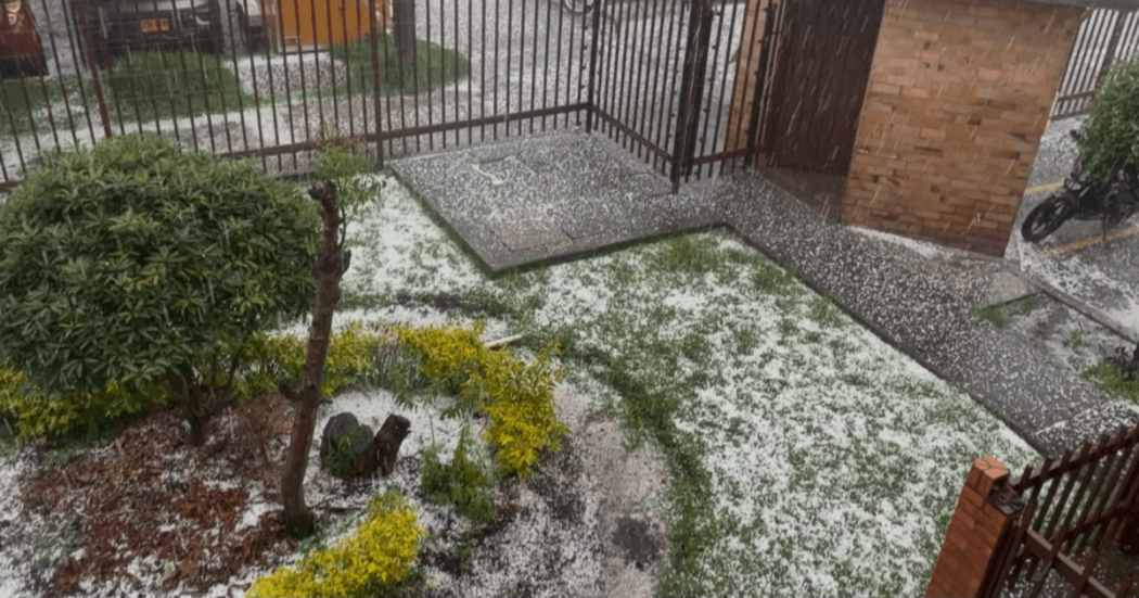 Granizada en Bogotá acumulada sobre el suelo de un patio con jardineras, mientras una estructura metálica y una cerca permanecen rodeadas por la capa blanca.