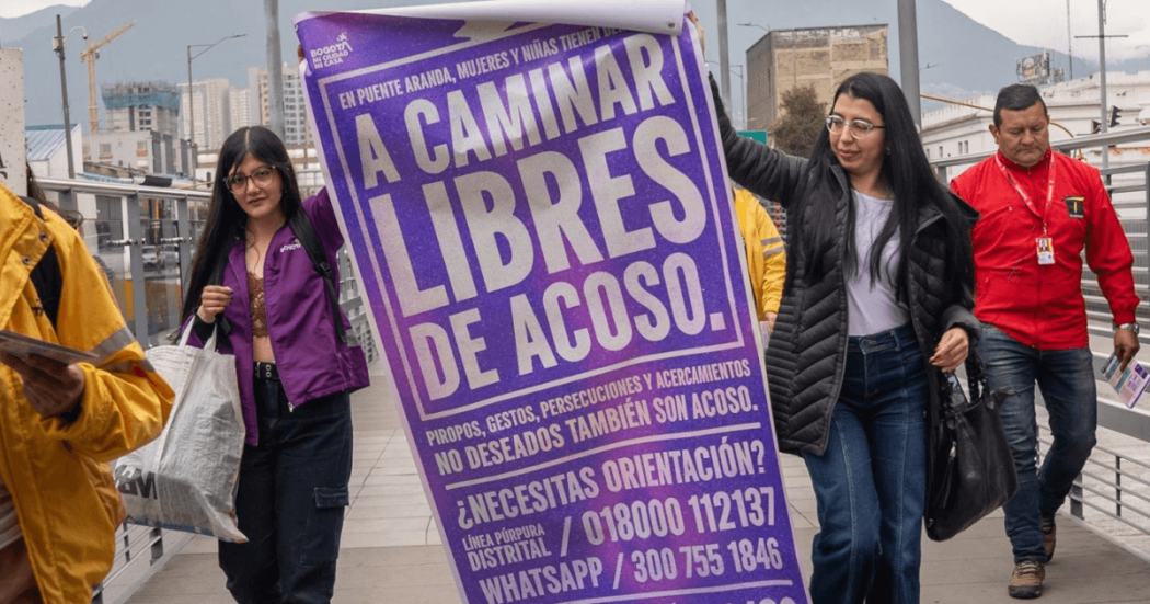Foto de dos mujeres cargando un cartel que dice "Mujeres y niñas tienen derecho a caminar libres de acoso".