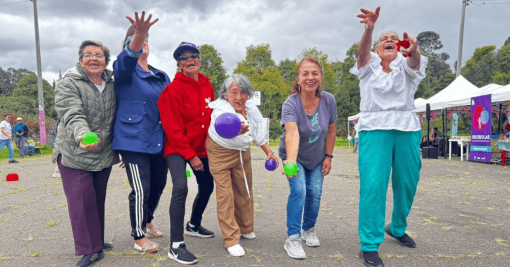 Grupo de personas participa en una actividad recreativa al aire libre; varias sostienen pelotas mientras avanzan por una zona verde.