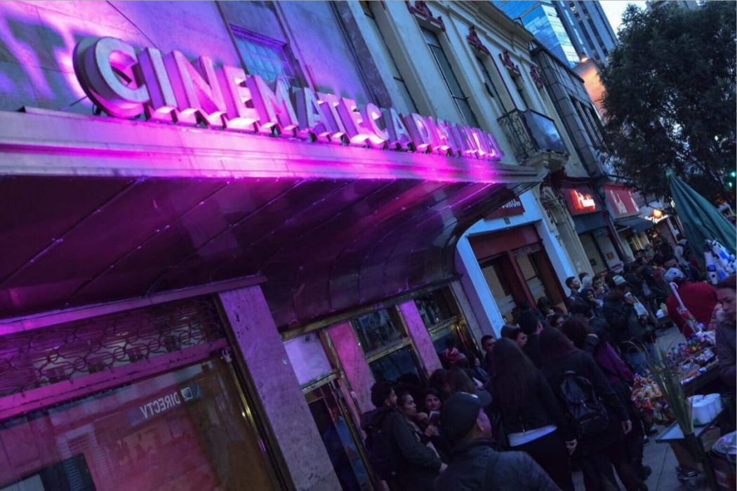 Fachada de la Cinemateca Distrital, una fila de personas en la entrada e iluminado con luz morada