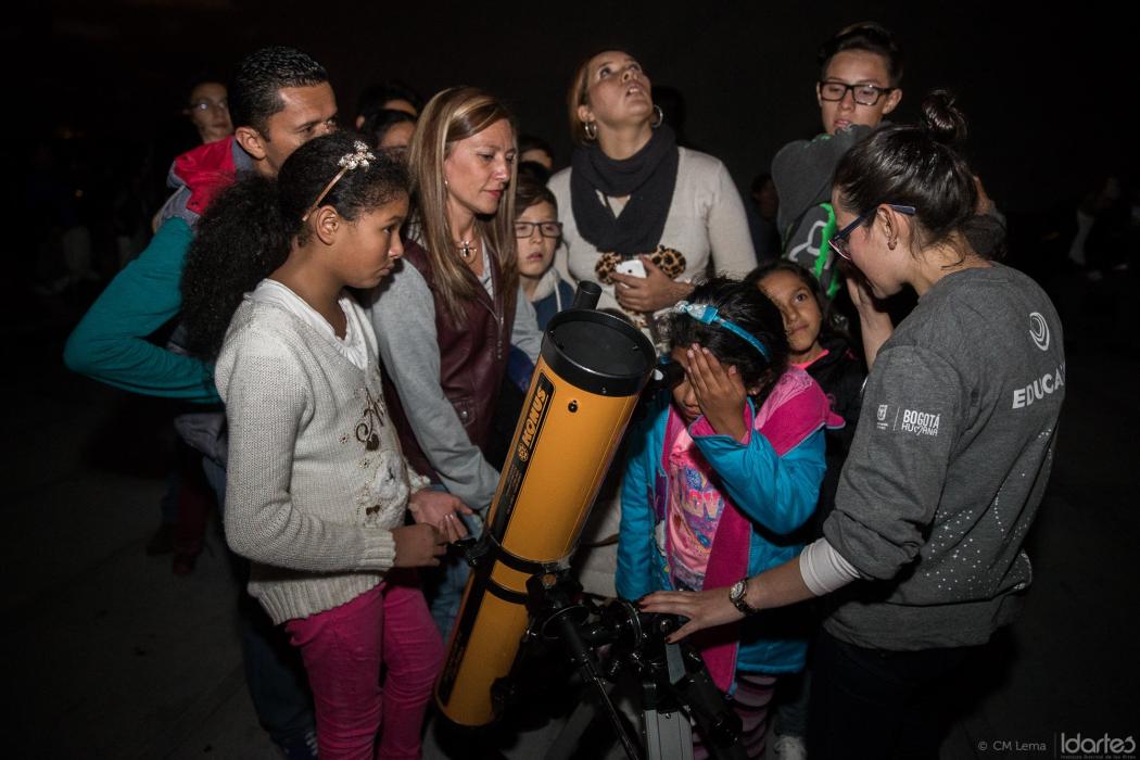 Varios niños y adultos alrededor de un telescopio observando hacia el cielo.