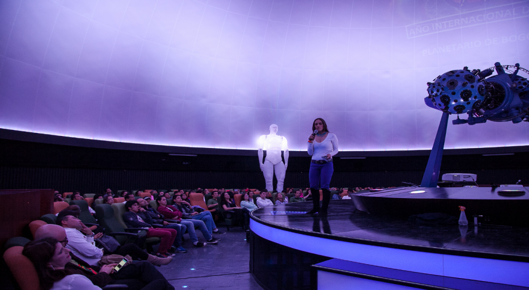 Una mujer hablando por el micrófono en el domo del Planetario, con publico