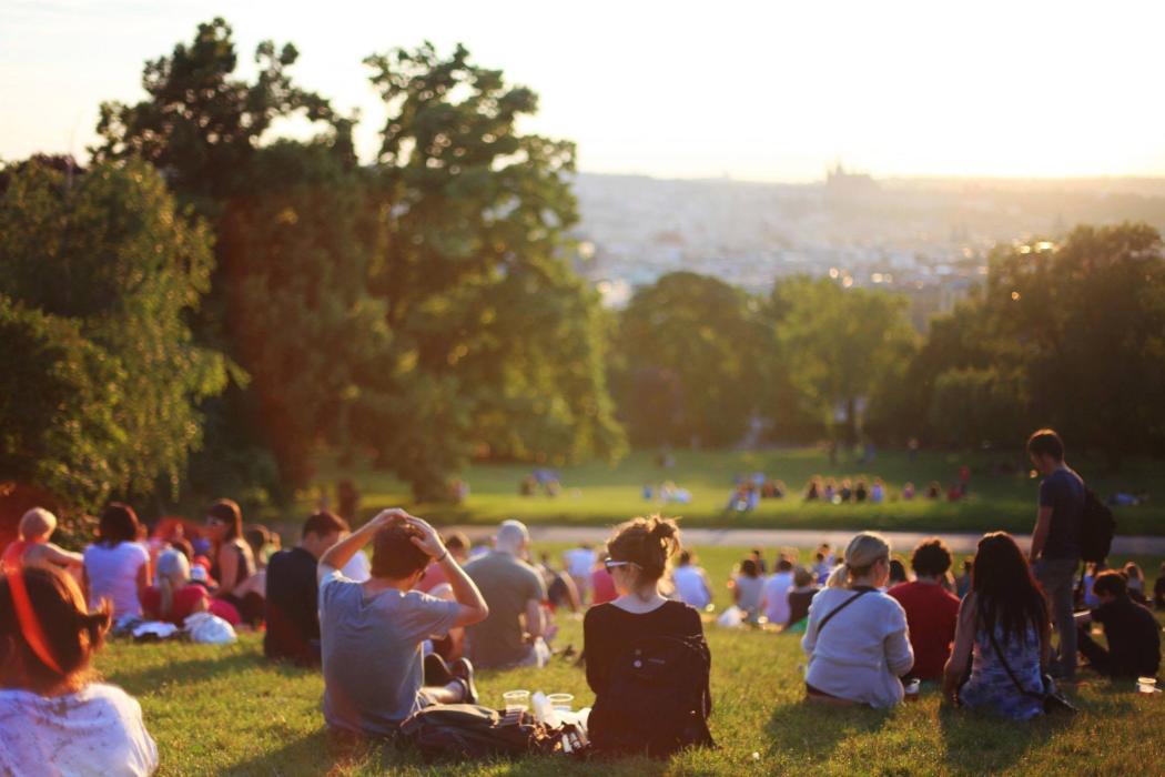 En un parque grande lleno de pasto hay varias personas sentadas compartiendo un picnic con la puesta del sol