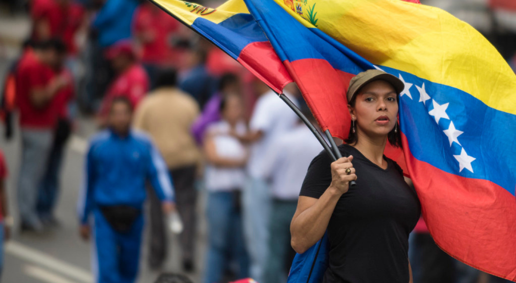 Joven de piel morena y cabello corto oscuro sostiene dos banderas de Venezuela. Foto: Eneas de Troya/Flickr