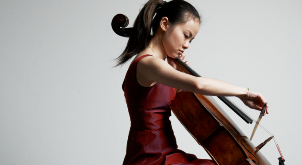 Una mujer joven, de rasgos asiáticos y pelo castaño toca el violonchelo.