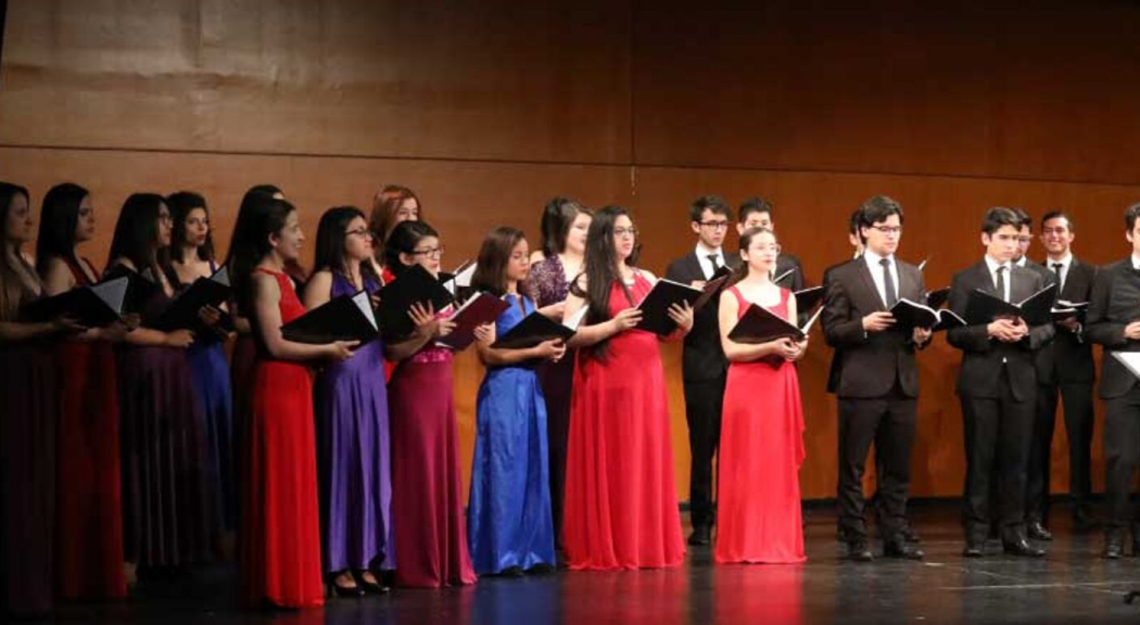 Un grupo de jóvenes vestidos formalmente cantan.