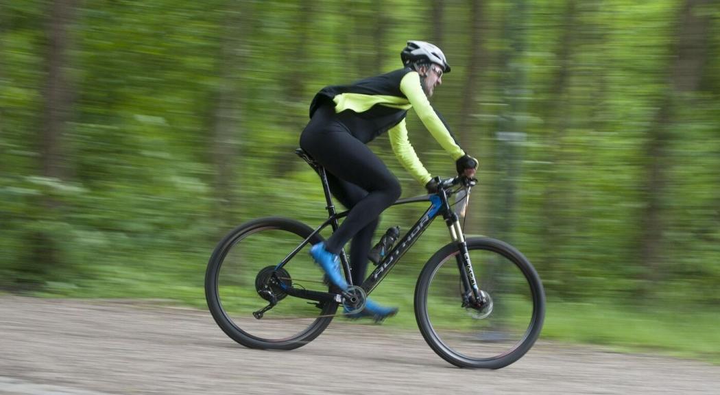 Hombre vestido de negro y verde a bordo de una bicicleta.