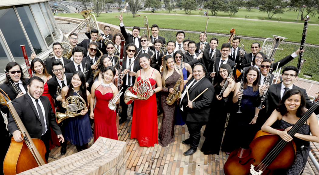 Jóvenes de la Orquesta Filarmónica Juvenil visten trajes formales y sostienen instrumentos musicales.