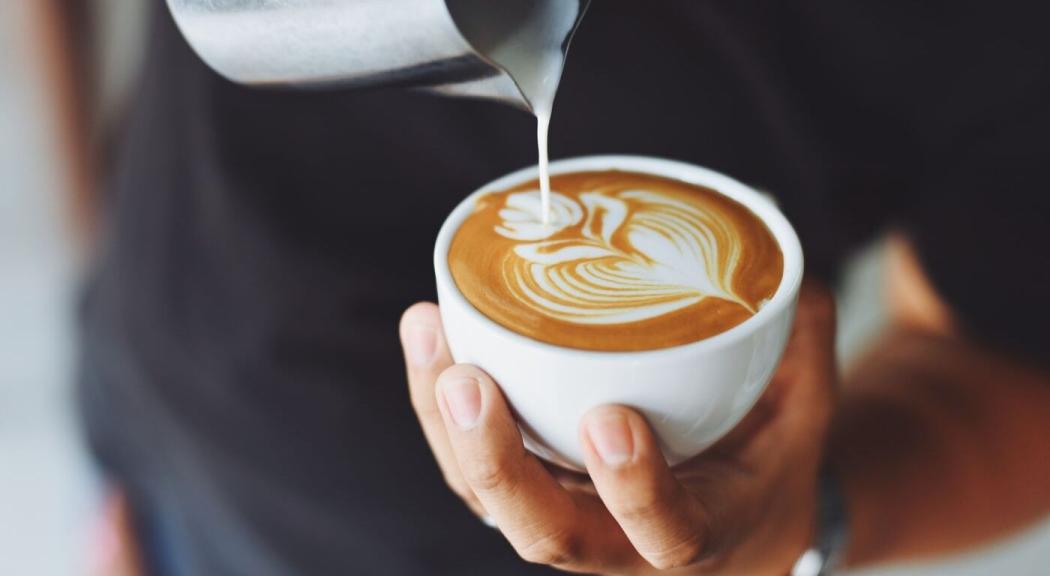 Un hombre preparar un café con un detalle de arte latte.