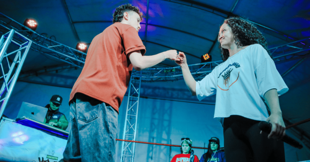 Imagen de dos jóvenes, hombre y mujere en escenario cantando