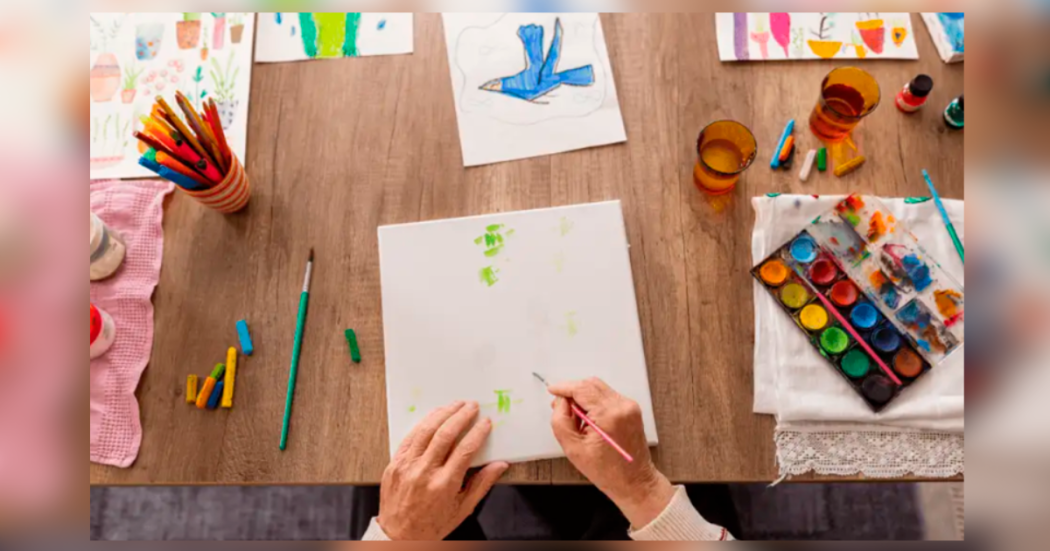 Imagen con manos de persona que se encuentra realizando proyecto de manualidades en mesa de madera con diversos materiales