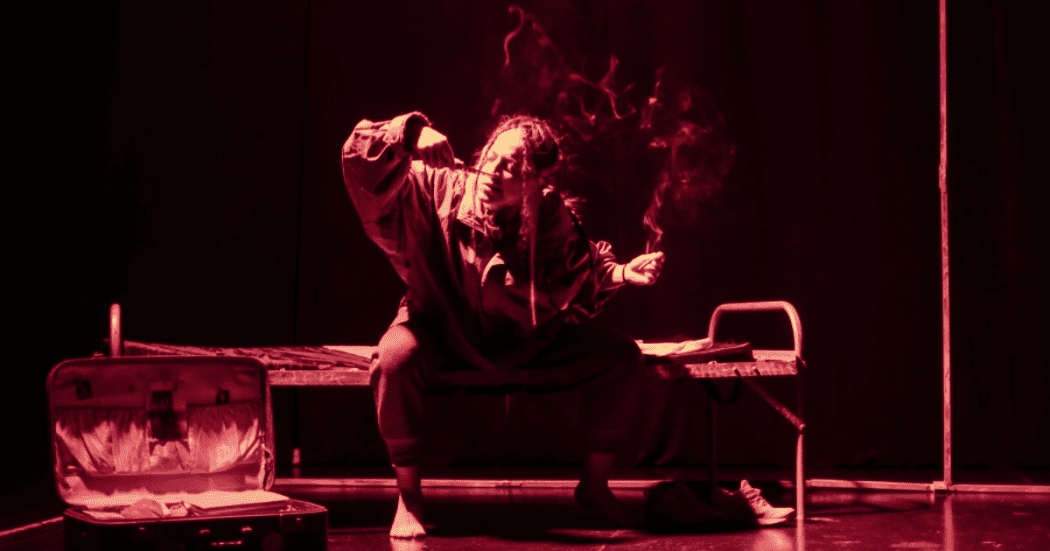 Imagen de mujer jóven sentada en una cama de reclusorio con algo en las manos que emite humo