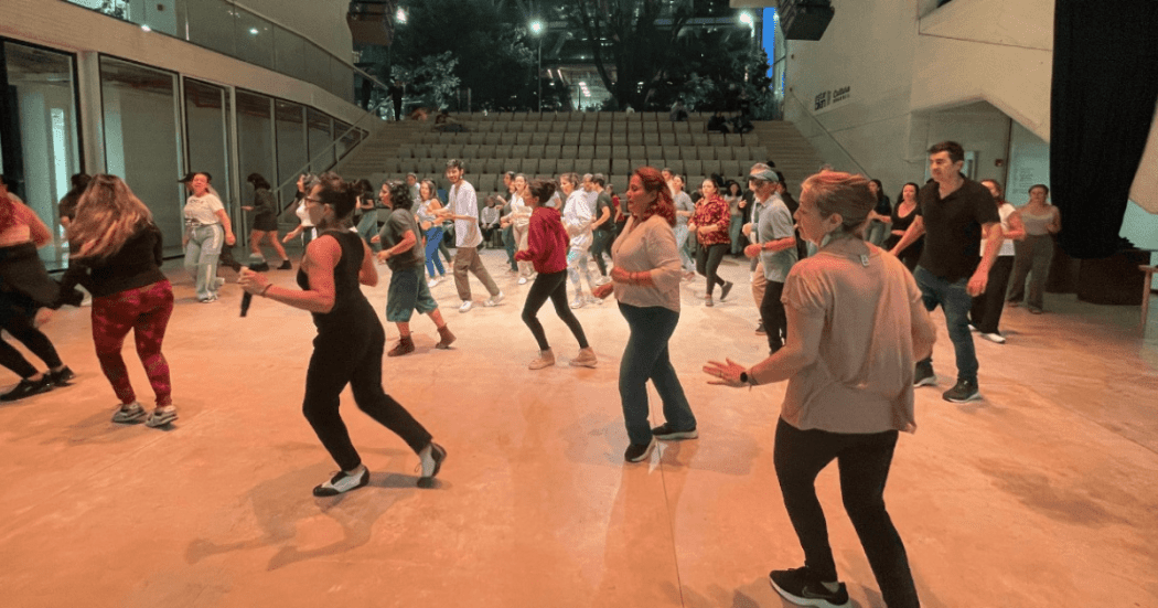 Imagen de un gran salón donde hay muchas personas tomando clases de baile 