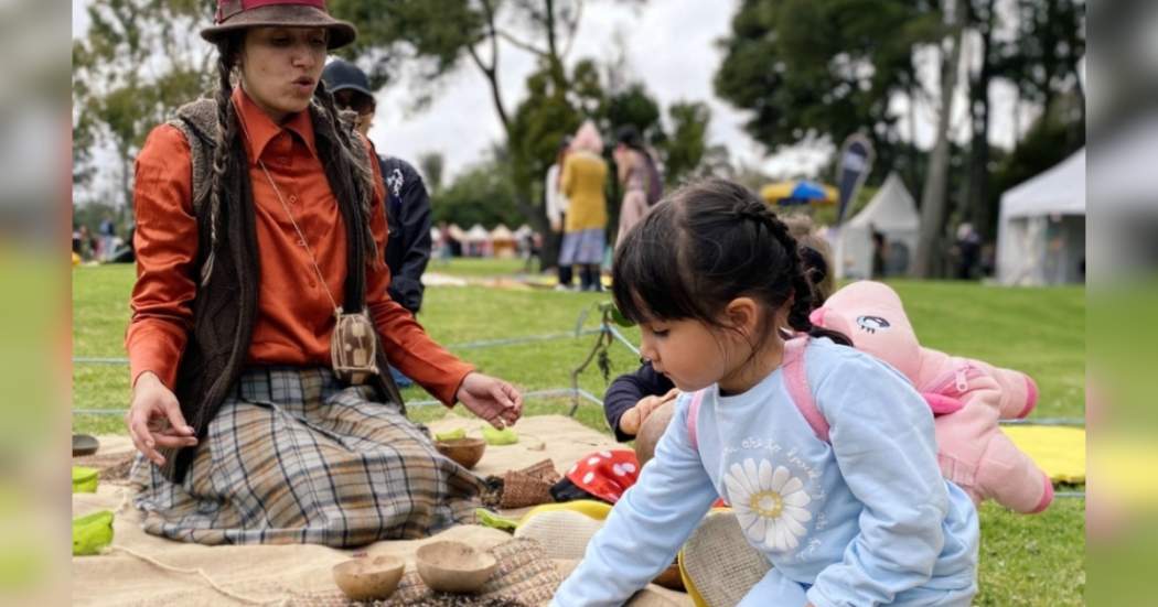 Imagen de una mamá y su hija sentada en un parque de picnic, de fondo se ve un parque y su naturaleza.