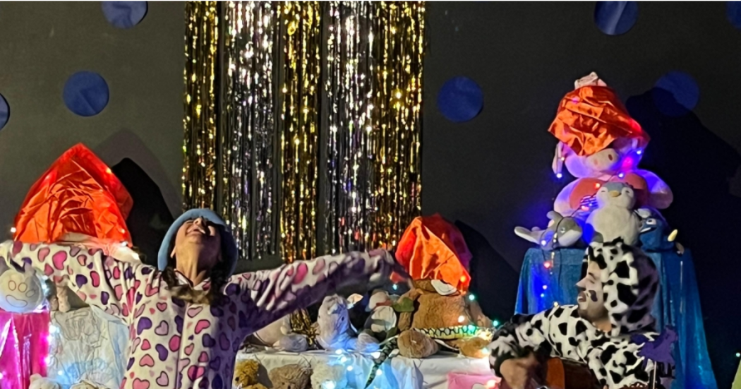 Imagen de los personajes de la obra en tarima donde se aprecia una mujer y un hombre en pijama con animales en peluche a su alrededor