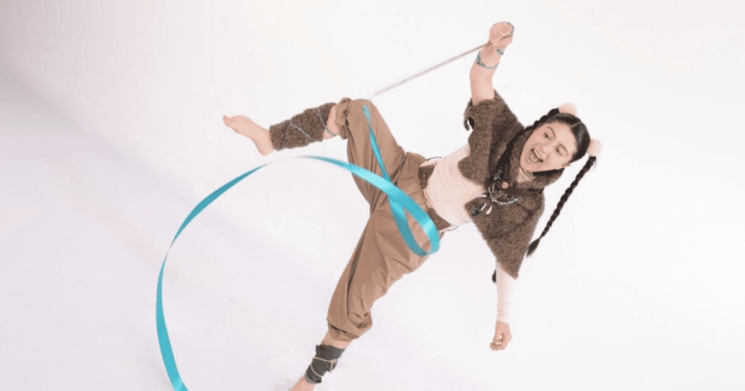 Imagen de una niña vestida de color café claro que juega con unas cintas de colores enredadas en sus manos