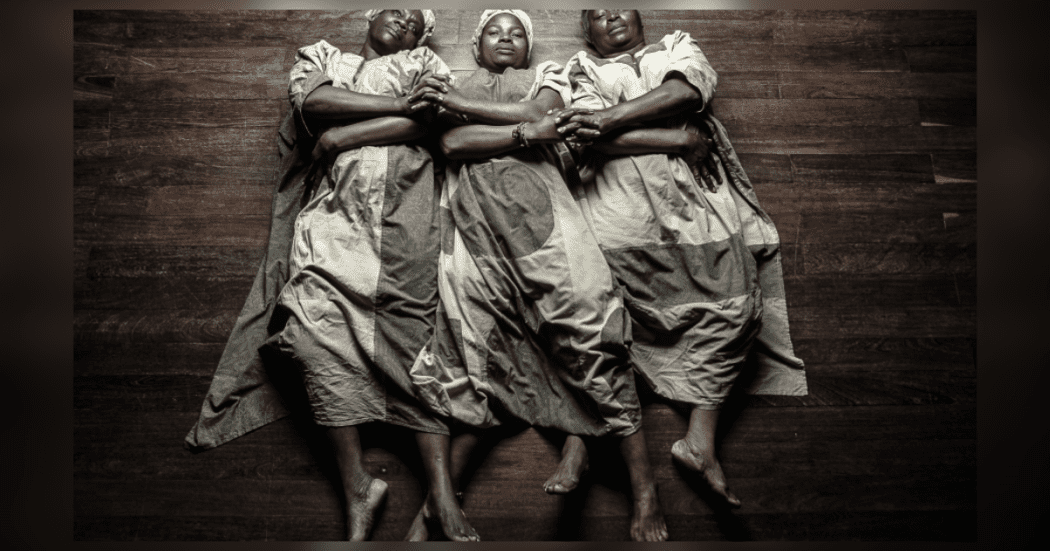Imagen de tres mujeres afrocolombianas acostadas y cogidas de las manos entrecurzadas